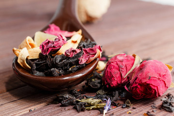 Composition of natural tea with a rose. Macro photo of tea petals on a ceramic spoon with a  rose. Tea with the ingredients of flowers and rose tea located on a wooden Board.