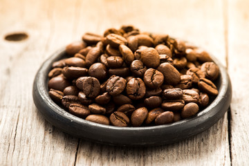 Roasted coffee beans on black plate on wooden background