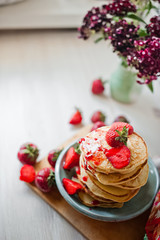 Stack of fritters with strawberries. Pancakes with red jam. Finished pancakes in the background