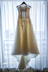 Wedding dress hanging on a hanger near window