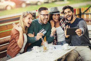 Friends having a coffee together. Two women and two men at cafe shopping on line with digital tablet