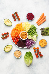 Vegetarian salad, top view of buddha bowl, various vegetables, carrot, courgette, cabbage, chickpeas, cucumber and tomatoes, on wooden board on white table, top view, selective focus