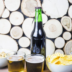 Dark beer in a bottle and light in glasses on a wooden table next to salty snacks - chips, peanuts and crackers