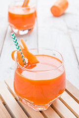 Fresh carrot juice in glass on a white wood table