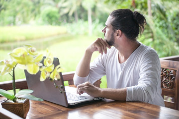 Freelance work on laptop. Man sitting at wooden desk inside garden working on computer
