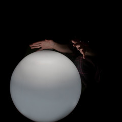 Two palms of the fortuneteller over a white, slightly illuminated ball in complete darkness