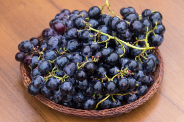 Ripe grapes in wicker basket on wooden table