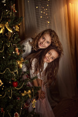 Two charming sisters look out from behind a Christmas tree in Christmas