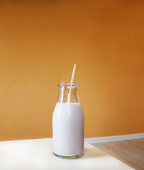 Milkshake with straw on white table and orange background