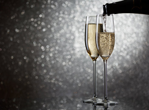 Image of bottle with champagne flowing in wine glasses on gray background
