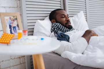 Unemotional ill man leaning on the white pillows