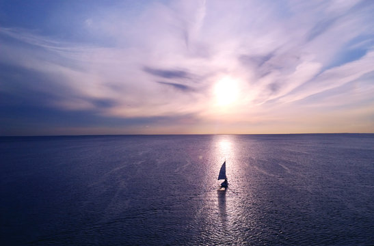 Romantic frame: yacht floating away into the distance towards the horizon in the rays of the setting sun. Purple-pink sunset