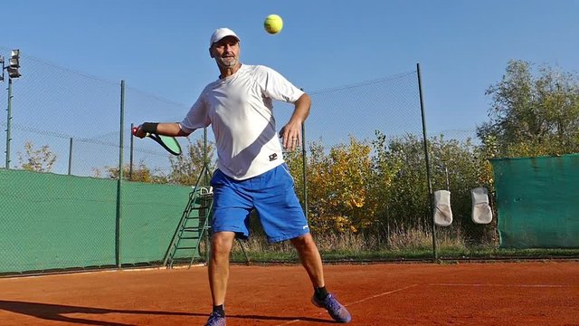 Mature man playing tennis on clay court, slow motion