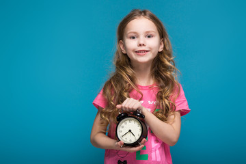 Pretty, little girl in tee shirt with brunet hair, with clock in hands