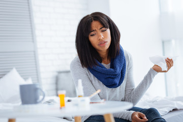 Unhappy young woman looking at the pills on her table
