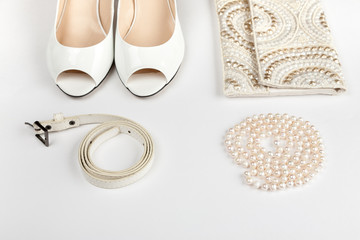 Female white shoes, bag, belt and pearl necklace on a white background