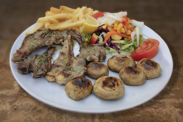 Lammkoteletts mit Pilze,  Pommes fites und Salat auf weißem Teller