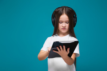 Beauty little girl in tee shirt and earphones with long hair hold tablet