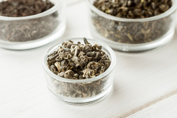 Different dry tea in a small glass dishes on a white wooden table