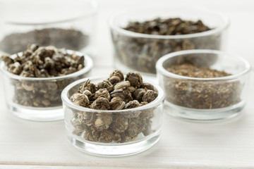 Different dry tea in a small glass dishes on a white wooden table