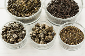 Different dry tea in a small glass dishes on a white wooden table