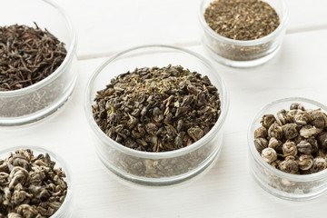 Different dry tea in a small glass dishes on a white wooden table