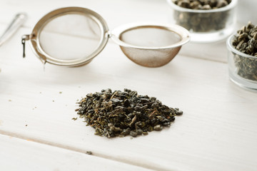 Metal strainer for tea with dry tea on a white wooden table