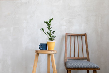 Simple interior with wooden chair and table with arranged flowerpot and cup on top.