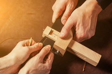 A close-up of a furrier and his assistant cuts a piece of leather to create a black belt on special equipment on a brown table, top view