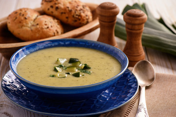 Cream soup with leek and zucchini on white wooden background.