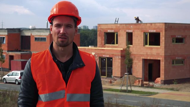 A young construction worker talks to the camera - a house under construction in the background