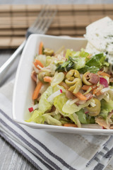 Fresh vegetables and bacon salad in a white bowl. A healthy iceberg salad with olives served on a wooden rustic table.