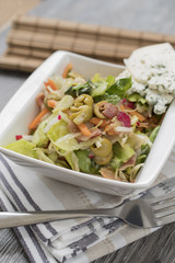 Fresh vegetables and bacon salad in a white bowl. A healthy iceberg salad with olives served on a wooden rustic table.