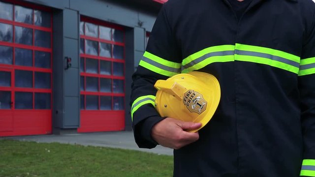 A firefighter stands in front of a fire station with his helmet on his side - closeup