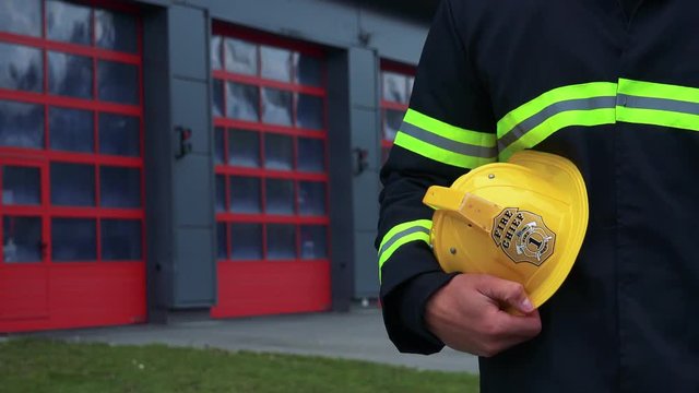 A firefighter stands in front of a fire station with his helmet on his side - closeup