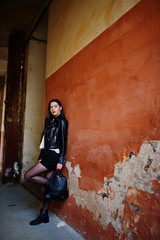 Fototapeta na wymiar Stylish brunette girl wear on leather jacket and shorts with backpack against orange wall.