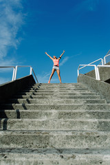 Happy female athlete raising arms to the sky for celebrating fitness or running workout goals and success.