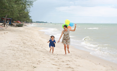 Mother and child girl running on the beach with colorful balloons. Holiday concept.
