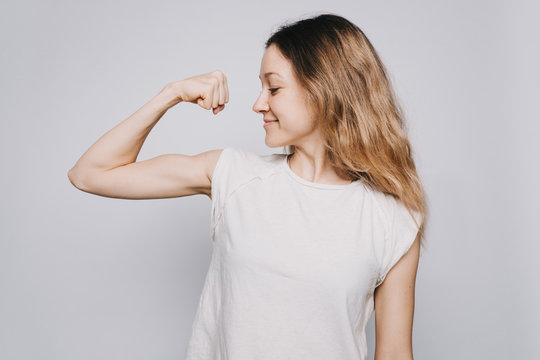 confident young sporty Caucasian woman in a white t-shirt showing biceps against white background