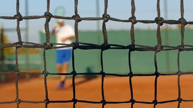 Man playing tennis on clay court, net in front, slow motion