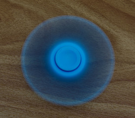 Pale blue fidget spinner spinning on a wood table top