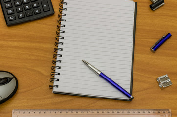 A blank notepad with copy space on a wood desk with office items around the edge