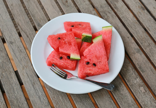 Fresh juicy watermelon slice on white plate on wooden table at restaurant.