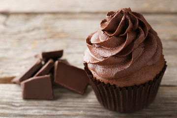 Tasty cupcake with pieces of chocolate on grey wooden table