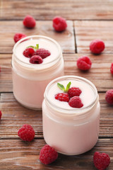 Raspberries yogurt in jars on brown wooden table