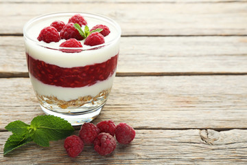 Dessert with raspberries and granola in glasses on grey wooden table