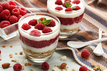 Dessert with raspberries and granola in glasses on white wooden table