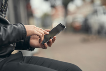 Close-up. The guy is holding a smartphone in his hands. On the street