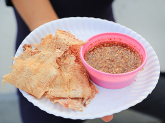 Mashed squid with sweet sauce on white paper plate in woman hand.