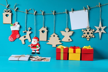 Christmas and New Year decorations made of plywood hanging on the rope. Christmas and New Year decorations with card and gift boxes on a light blue wooden background.